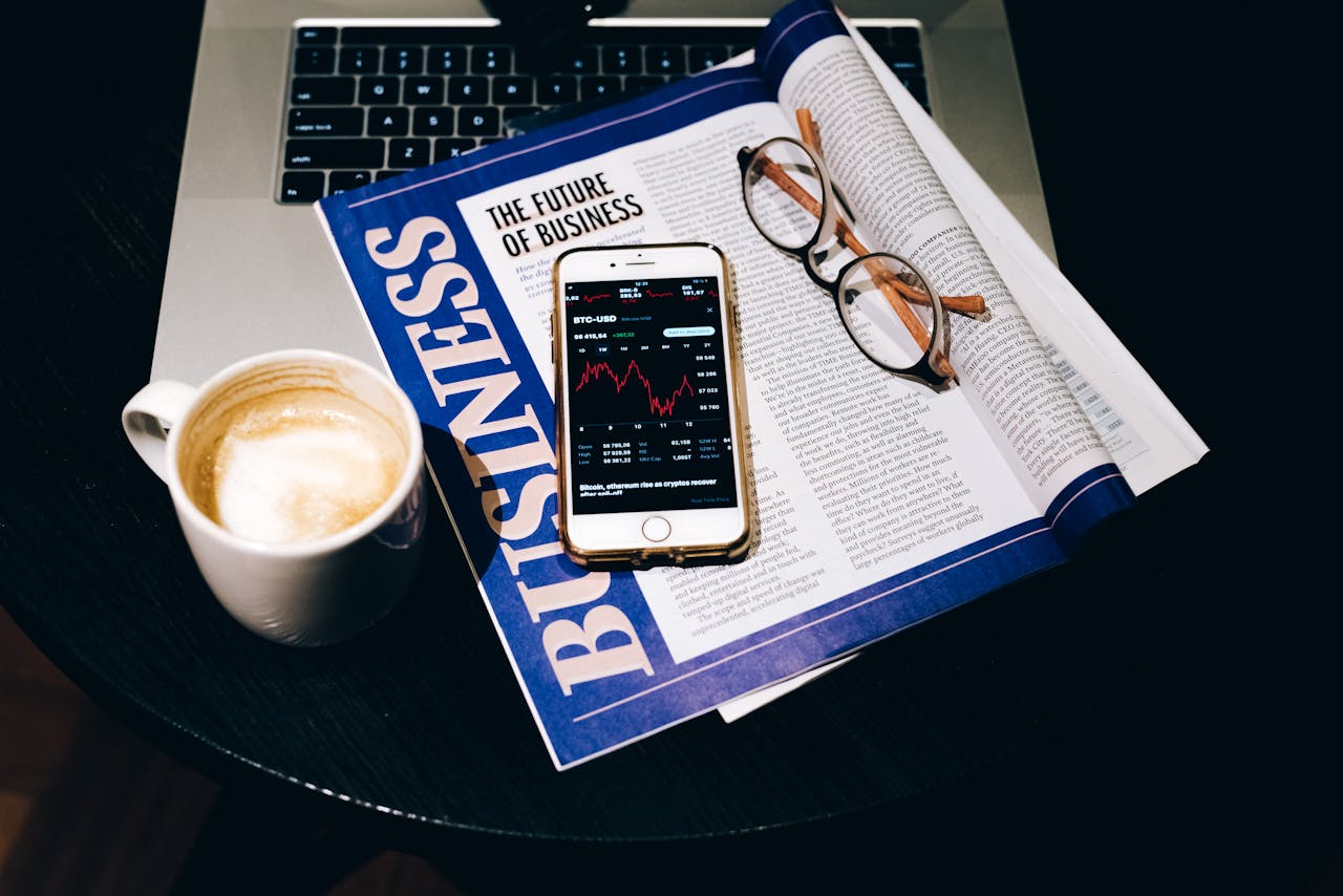 A business setup with a laptop, coffee, phone, and newspaper. Perfect for finance themes.
