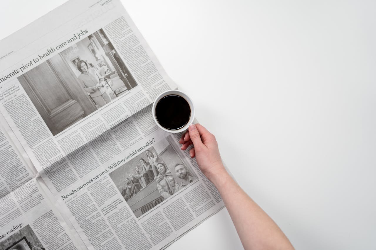 Hand holding a black coffee over newspaper, perfect for business and morning themes.